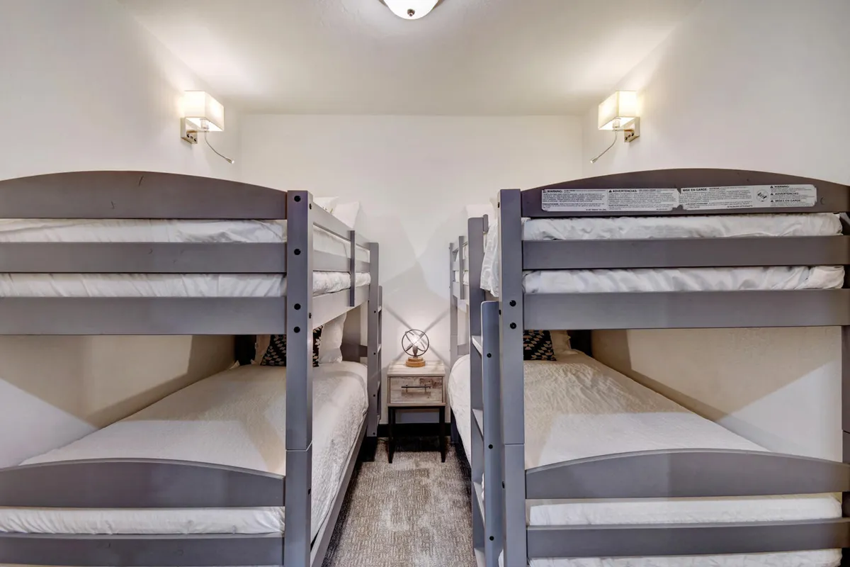 A playful bunk room with two sets of bunk beds, a nightstand, and wall sconces. The decor is youthful, inviting, and perfect for kids or groups, fostering a sense of adventure and camaraderie.