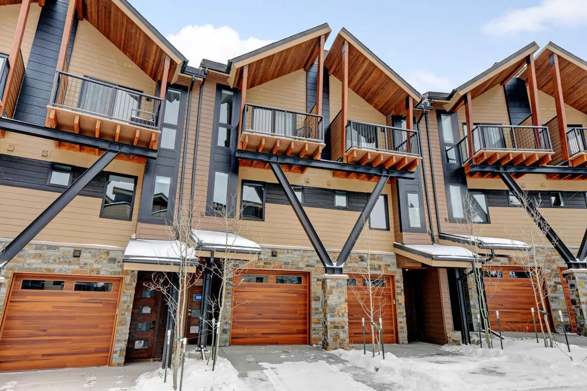 An exterior shot of a cozy property with wooden balconies, a stone facade, garage doors, and a snow-covered ground. The mood is inviting, hinting at wintertime gatherings, après-ski fun, and outdoor exploration.