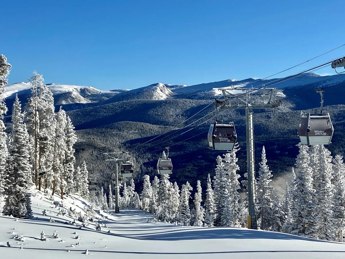 A breathtaking view of ski lift gondolas rising above snow-covered trees with mountains in the background. The scene suggests both leisure and thrill, inviting guests to explore the slopes and scenic beauty of Winter Park.