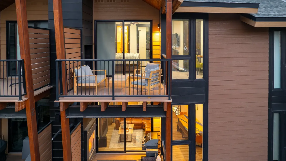 A warmly lit exterior shot featuring a balcony with inviting outdoor furniture, large windows shining with interior light, and a view that frames the home as both welcoming and connected to its surroundings. The setting is ideal for evening gatherings or relaxing under the stars.