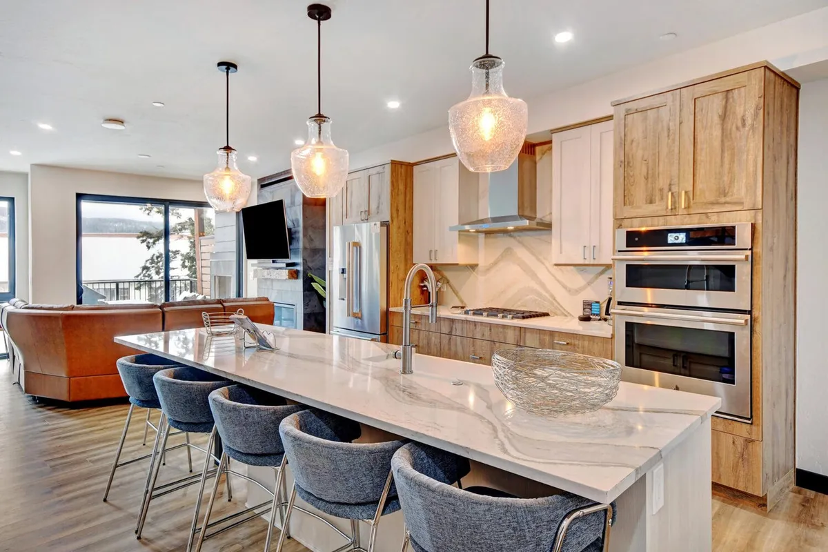 A modern kitchen with a large island countertop, stylish bar stools, state-of-the-art appliances, and expansive windows letting in natural light. The space is open and welcoming, designed for cooking, entertaining, and family gatherings.