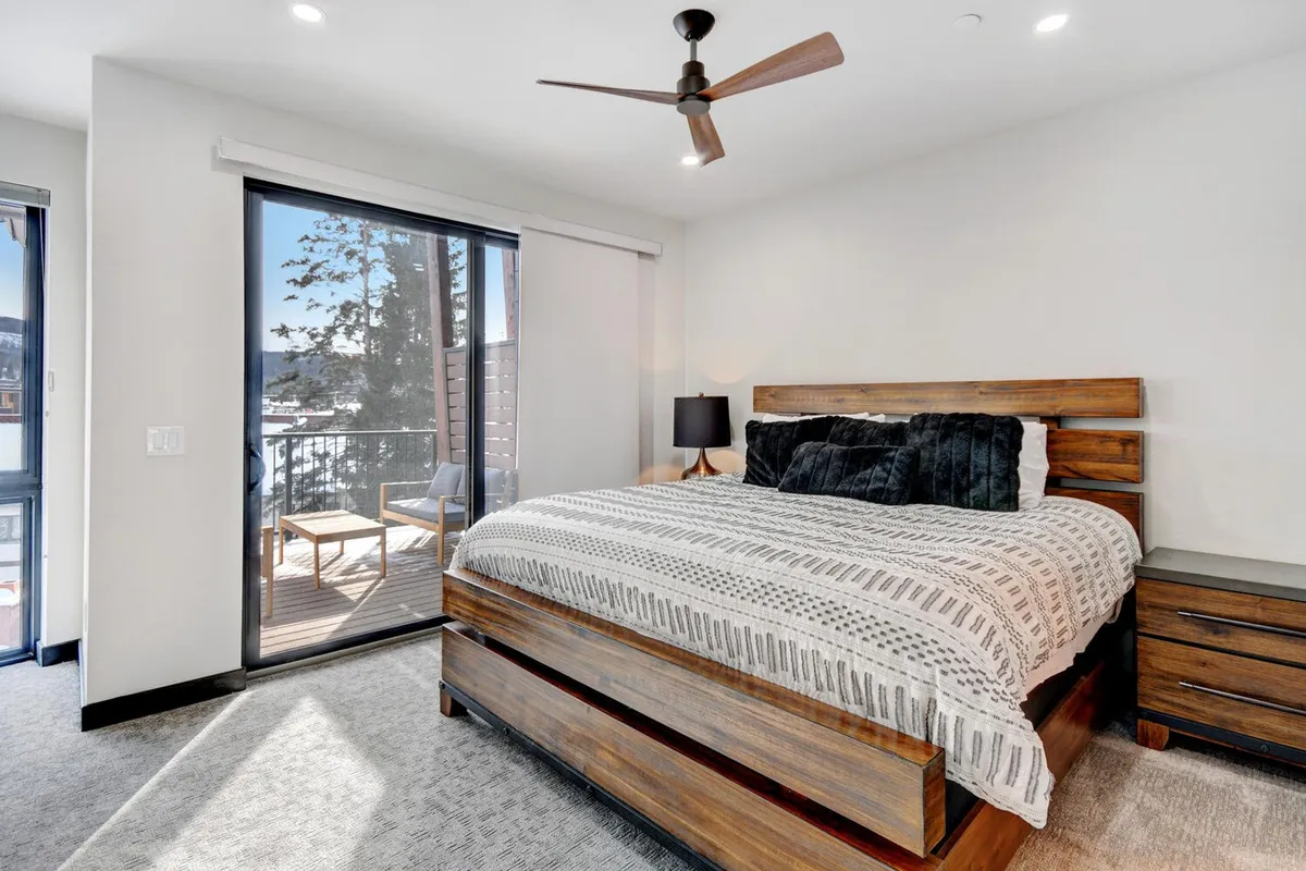 A serene interior bedroom scene with a bed positioned next to a window and a door leading to an outdoor deck. The deck is visible, inviting thoughts of morning coffee or sunset relaxation right outside the private suite.