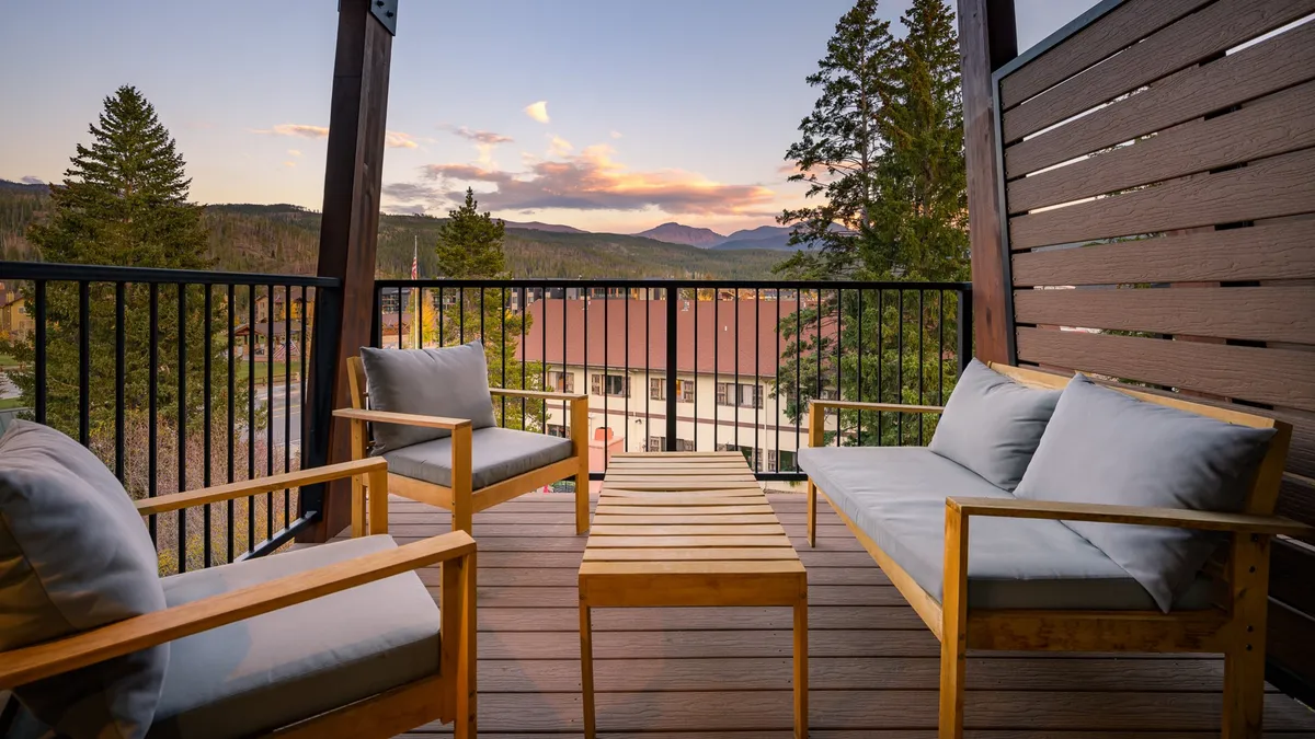 A scenic view from a deck or patio, featuring comfortable wooden seating and a breathtaking panorama of mountains at sunset. The atmosphere is serene and inviting, ideal for morning coffee or evening relaxation, and highlights the connection between the home and its natural surroundings.